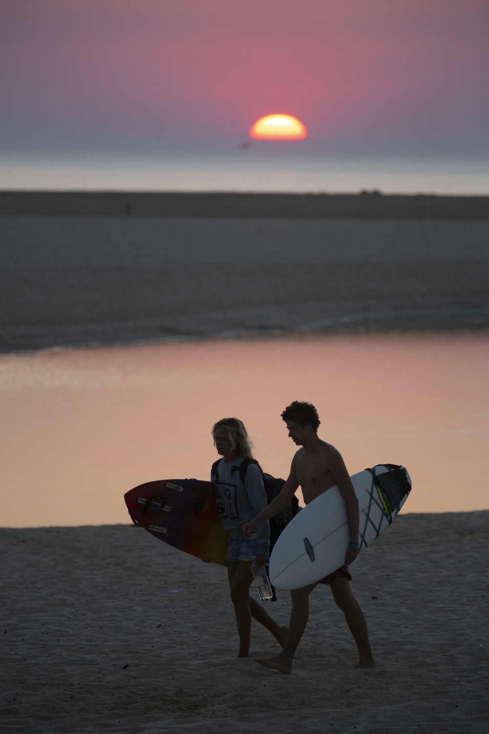 Surferpärchen geht im Abendrot mit Surfbrettern unterm Arm nach Hause